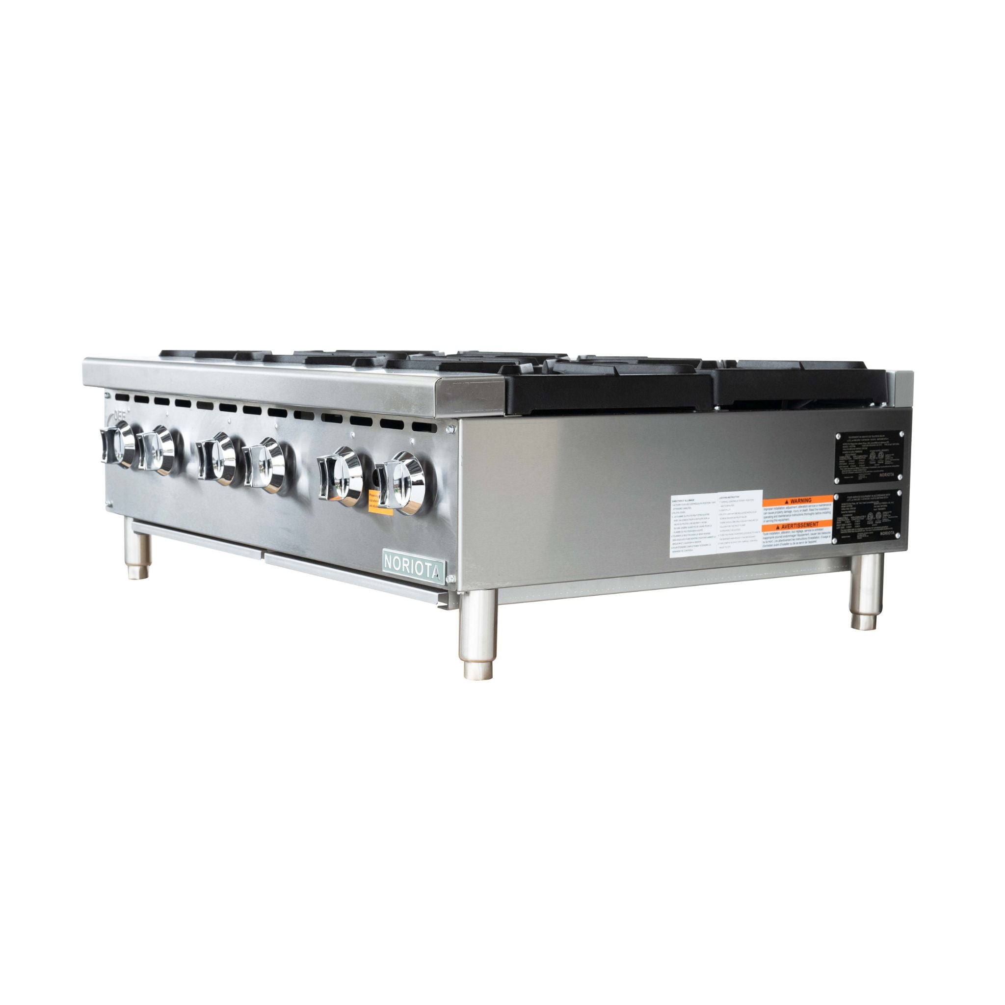 A commercial gas hot plate with a stainless steel body, black cast iron burner grates on top, and silver legs, featuring a yellow warning label on the front.